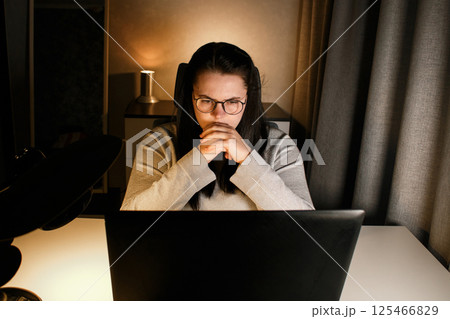Young woman with eyeglasses working on laptop at home late at night, using modern technologies and getting online education. Remote learning concept. Online university. Focus on process. 125466829