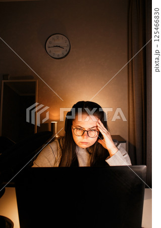 Female remote worker sitting in home office and working on online project using laptop. Woman in eyeglasses watching on computer screen and gathering information. Female remote worker sitting in home office and working on online project using laptop. Woman in eyeglasses watching on computer screen and gathering information. 125466830
