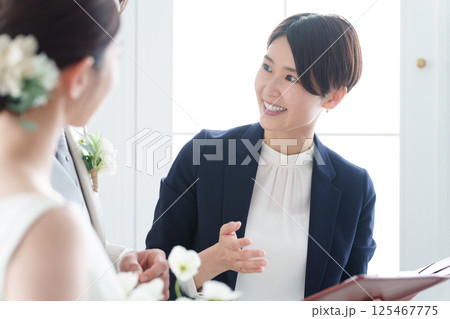 新郎新婦と話す結婚式場スタッフ 125467775
