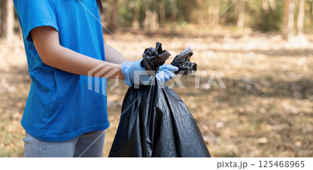 Volunteer holding a garbage bag in a forest, showcasing commitment to environmental cleanup and community service Volunteer holding a garbage bag in a forest, showcasing commitment to environmental cleanup and community service 125468965