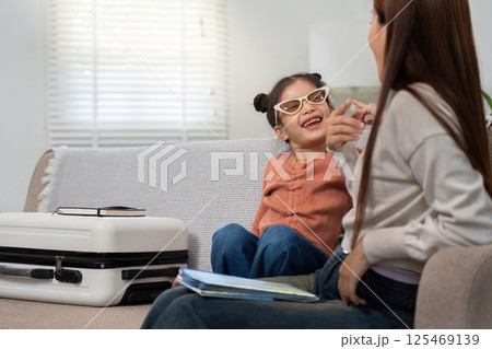 Joyful Moments in Travel Planning. A cheerful girl shares a laugh with her mother while packing. 125469139