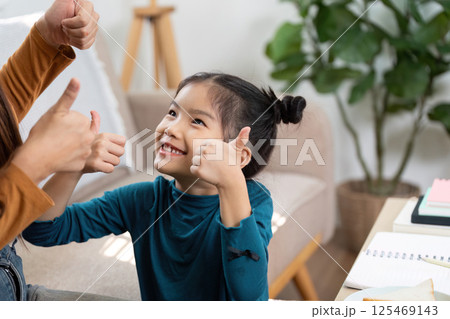 Positive Reinforcement and Happiness. A girl joyfully engages in a thumbs-up gesture while learning at home. 125469143