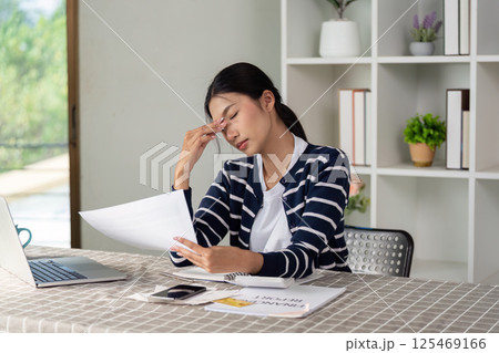 Stressed woman reviewing bills at home, managing finances with a laptop. 125469166