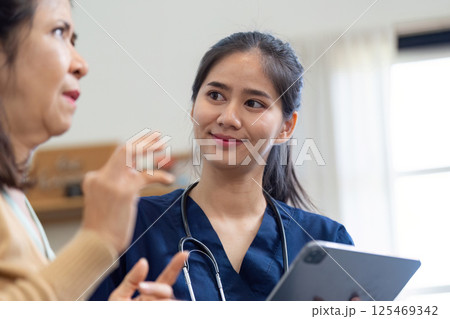 Caregiver engaging in conversation with elderly patient while using a tablet 125469342