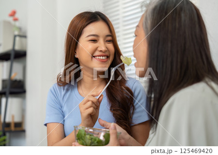 Wellness and Nutrition. A daughter playfully feeding her mother a healthy salad while enjoying their time together. Wellness and Nutrition. A daughter playfully feeding her mother a healthy salad while enjoying their time together. 125469420