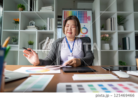 Graphic designer presenting color scheme options while sitting at her desk in a modern creative workspace Graphic designer presenting color scheme options while sitting at her desk in a modern creative workspace 125469466