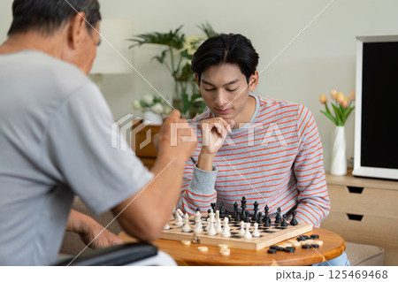 Young man and his father playing chess at home, enjoying family time. Young man and his father playing chess at home, enjoying family time. 125469468