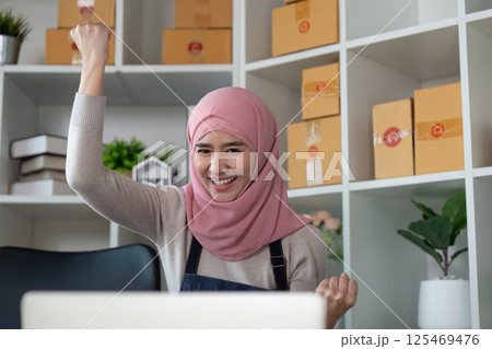 Joyful Muslim woman celebrating success in her online business, showcasing positivity and achievement. 125469476