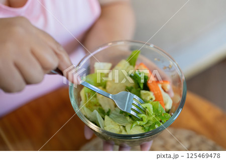 Focused overweight woman preparing to enjoy a fresh salad as part of her weight loss journey 125469478