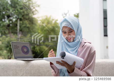 Muslim business woman in hijab reviewing documents and smiling outdoors. Muslim business woman in hijab reviewing documents and smiling outdoors. 125469566