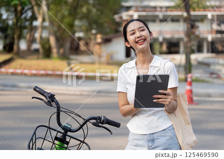 Sustainable Living and Technology. A woman engaging with her tablet while stopped on her bicycle. 125469590