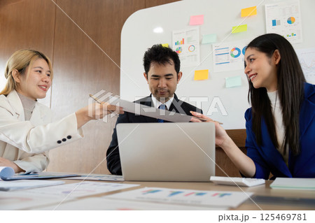 Team members exchanging documents in a meeting, highlighting cooperation and teamwork in the workplace. 125469781