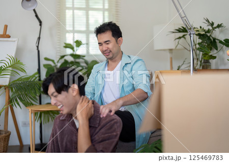 LGBTQ couple sharing a laugh during a massage while settling into their new home. 125469783