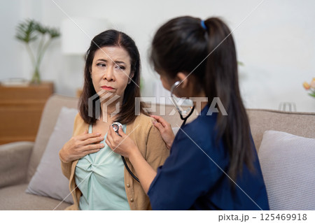 Caregiver using stethoscope on elderly patient, assessing health condition. Caregiver using stethoscope on elderly patient, assessing health condition. 125469918