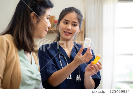 Empathetic caregiver explaining medication use to elderly patient in a home setting 125469984