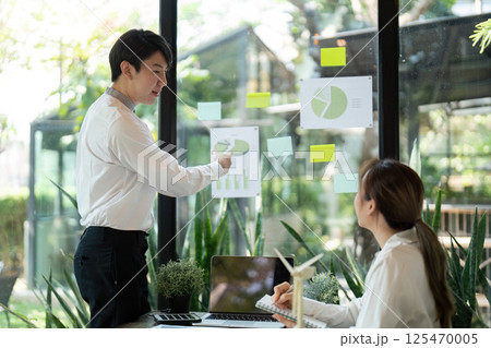 Sustainability and Leadership. A professional presenting renewable energy strategies to colleagues in an eco-conscious environment. Sustainability and Leadership. A professional presenting renewable energy strategies to colleagues in an eco-conscious environment. 125470005