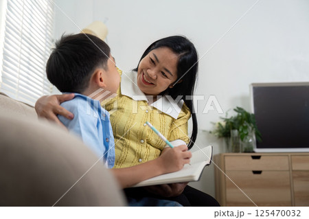 Mother and Son Learning Together. A mother joyfully assists her son with his studies, creating a nurturing atmosphere. Mother and Son Learning Together. A mother joyfully assists her son with his studies, creating a nurturing atmosphere. 125470032