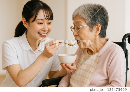 介護士が高齢女性に食事を介助する風景 介護士が高齢女性に食事を介助する風景 125473499