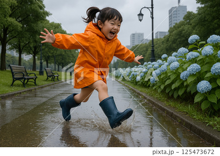 雨の公園で紫陽花の横を跳ねるレインコート姿の日本人少女 125473672
