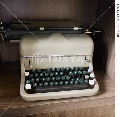 There is an old typewriter on a wooden shelf. The typewriter has a vintage look. 125474704