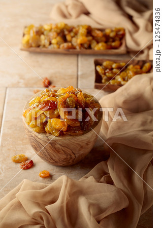 Yellow sultana raisins in a wooden bowl on a beige background. 125474836