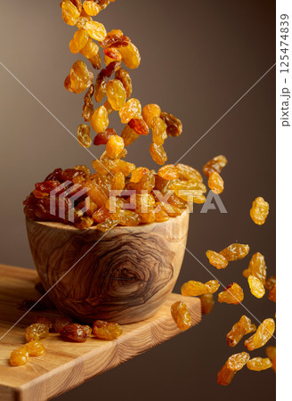 Yellow sultana raisins pour into a wooden bowl. 125474839