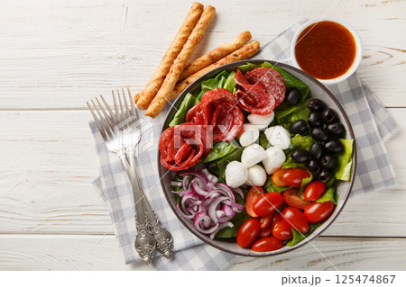 Pizza bowl salad with salami sausages, mozzarella cheese, tomatoes, olives, onions, romaine lettuce and spicy dressing served with breadsticks. Horizontal top view Pizza bowl salad with salami sausages, mozzarella cheese, tomatoes, olives, onions, romaine lettuce and spicy dressing served with breadsticks. Horizontal top view 125474867