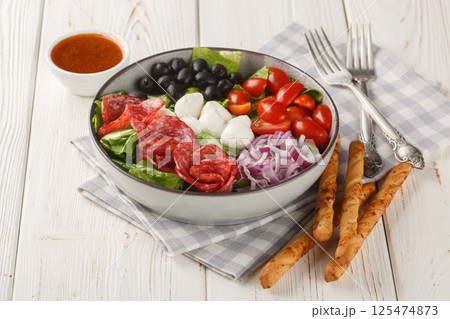 Pizza bowl salad with salami sausages, mozzarella cheese, tomatoes, olives, onions, romaine lettuce and spicy dressing served with breadsticks close-up. Horizontal Pizza bowl salad with salami sausages, mozzarella cheese, tomatoes, olives, onions, romaine lettuce and spicy dressing served with breadsticks close-up. Horizontal 125474873