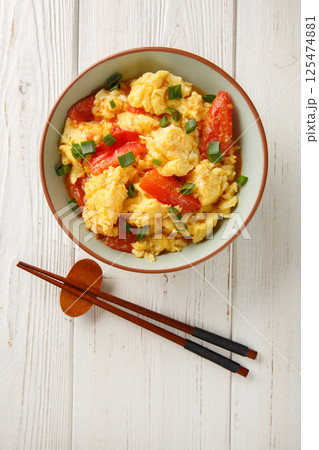 Soft silky eggs stir fried in a sweet tangy tomato sauce with green onions closeup on the plate. Vertical top view Soft silky eggs stir fried in a sweet tangy tomato sauce with green onions closeup on the plate. Vertical top view 125474881
