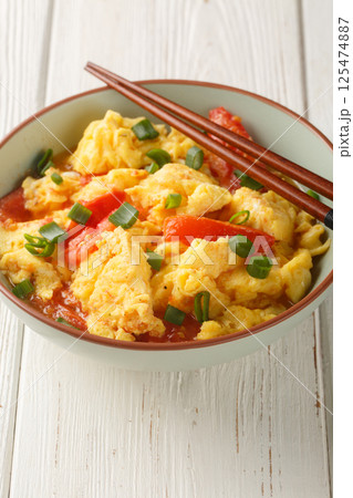 Soft silky eggs stir fried in a sweet tangy tomato sauce with green onions closeup on the plate. Vertical 125474887