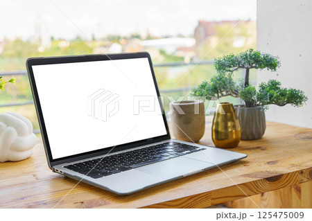 Laptop computer with white screen on wooden desk on window background. Mockup, template, copy space 125475009