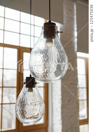 Decorative lamps, chandelier made of textured glass in loft living room on large window background Decorative lamps, chandelier made of textured glass in loft living room on large window background 125475036