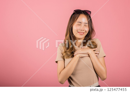 Beauty Asian young woman touching her chest for thanking in studio shot isolated on pink background, happy charming female smiling hold hands chest near heart honest with grateful gesture 125477455