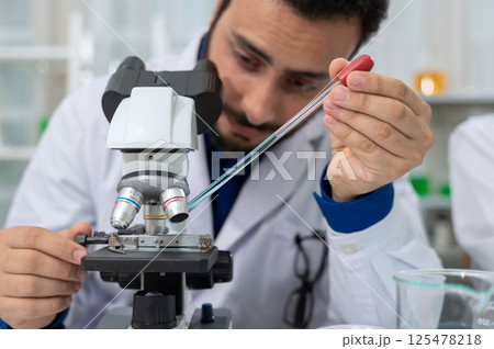 Male scientist dropping chemical liquid on slide at microscope. Science and Technology concept 125478218