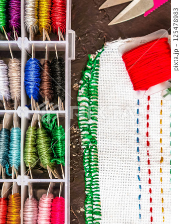 Set of multi-colored cotton threads and fragment of colorful cross-stitch embroidere. Colorful mouline threads. Top view Set of multi-colored cotton threads and fragment of colorful cross-stitch embroidere. Colorful mouline threads. Top view 125478983