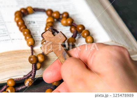 Hand holding and praying on rosary, on Bible background Hand holding and praying on rosary, on Bible background 125478989