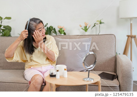 Beauty and Age Diversity. A senior woman applying skincare while combing her hair. Beauty and Age Diversity. A senior woman applying skincare while combing her hair. 125479135