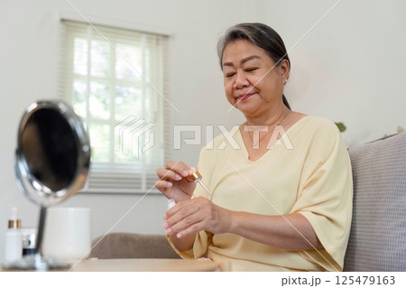 Beauty and Self-Care. An elderly woman applying serum, enjoying her skincare routine at home. Beauty and Self-Care. An elderly woman applying serum, enjoying her skincare routine at home. 125479163
