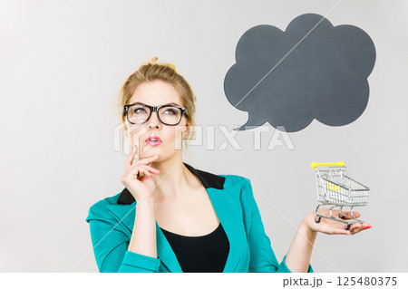 Thinking business woman holding small tiny shopping cart Thinking business woman holding small tiny shopping cart 125480375