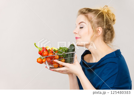 Woman holds shopping basket with vegetables, smelling 125480383