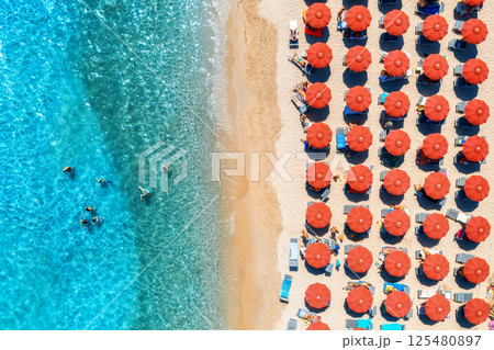 Aerial view of colorful umbrellas on beach, people in blue sea Aerial view of colorful umbrellas on beach, people in blue sea 125480897