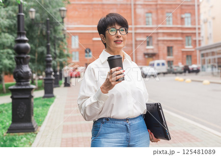 Mature woman with coffee and laptop standing outdoors. Freelance work, career focus and independent lifestyle 125481089