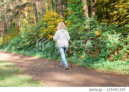 Senior woman doing nordic walking on autumn forest trail. Active lifestyle, health and wellness in retirement years Senior woman doing nordic walking on autumn forest trail. Active lifestyle, health and wellness in retirement years 125481191