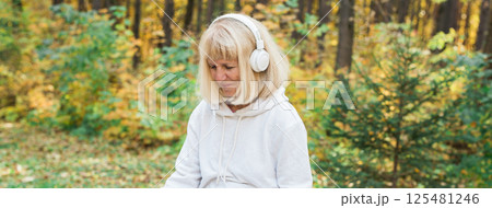 Banner senior woman enjoying music in the autumn forest, copy space. Relaxation, happiness, mindfulness and connection with nature during active aging 125481246