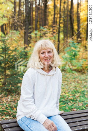 Senior woman relaxing on a bench in an autumn park. Concept of aging gracefully, wellbeing, emotional calmness, leisure and joy of simple outdoor pleasures 125481509