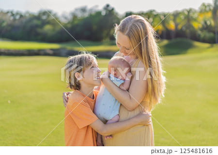 Mother, older son, and newborn baby on a meadow in the park. Family spending quality time together in nature. Parenthood, love, and family bond concept 125481616
