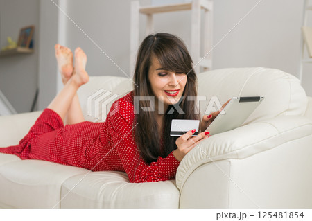 Woman uses credit card and tablet to shop online from home sofa. Digital commerce, consumer ease and modern shopping 125481854