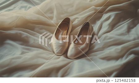 Beige ballet shoes lay on a sheer light-colored fabric 125482158