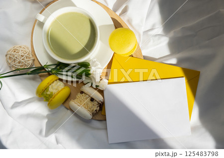Empty white envelope letter mockup template Green latte match and macaron on messy bed. Concept of holiday breakfast morning tea drink. Cozy minimalist superfood vibrant colors healthy eating. Organic 125483798