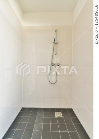 A sleek, contemporary shower stall featuring clean lines and a spacious design, accented by tiled walls and a stainless steel showerhead. 125485616